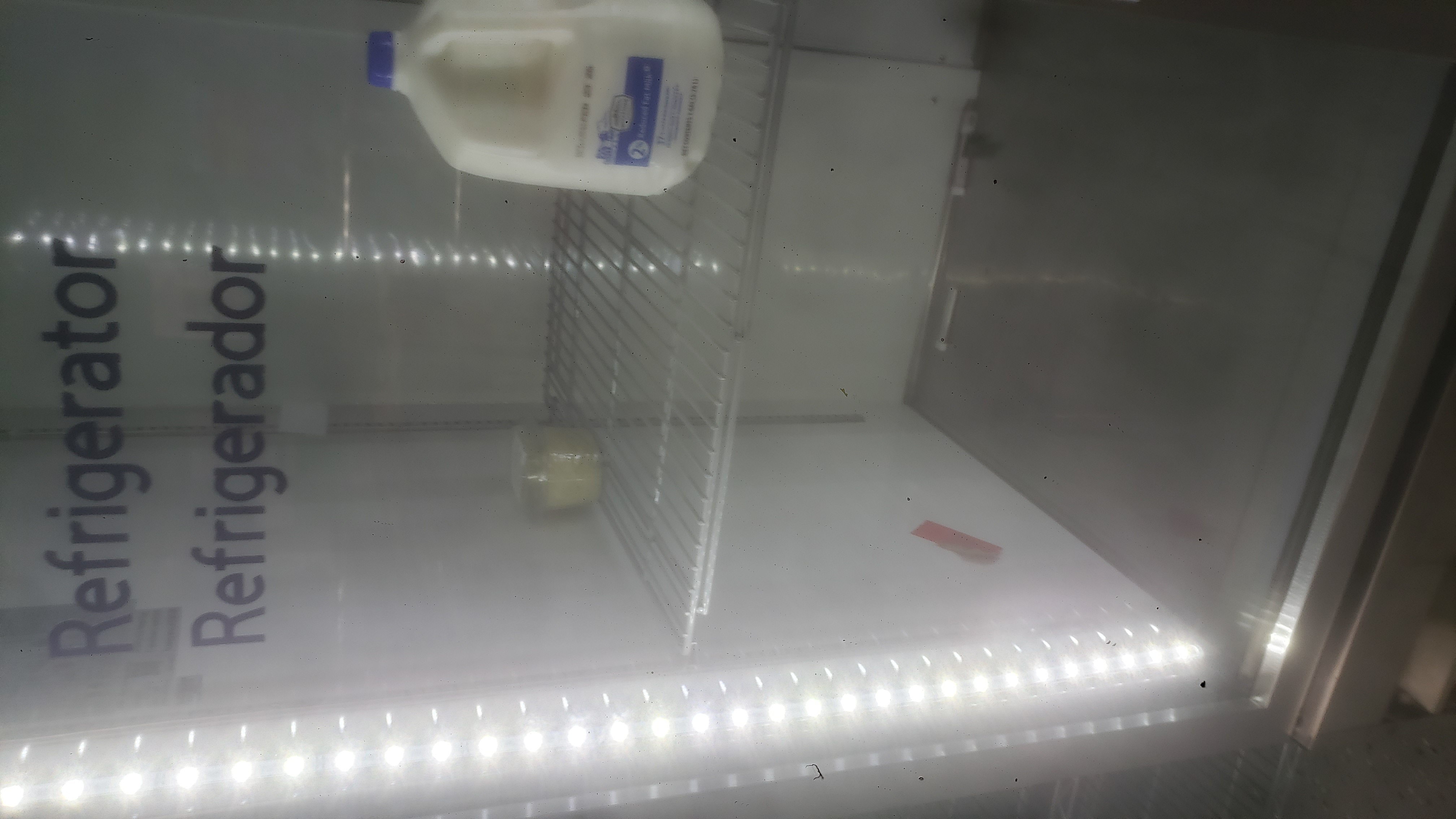 Gallon of milk and container of chopped onions on shelf in a fridge.